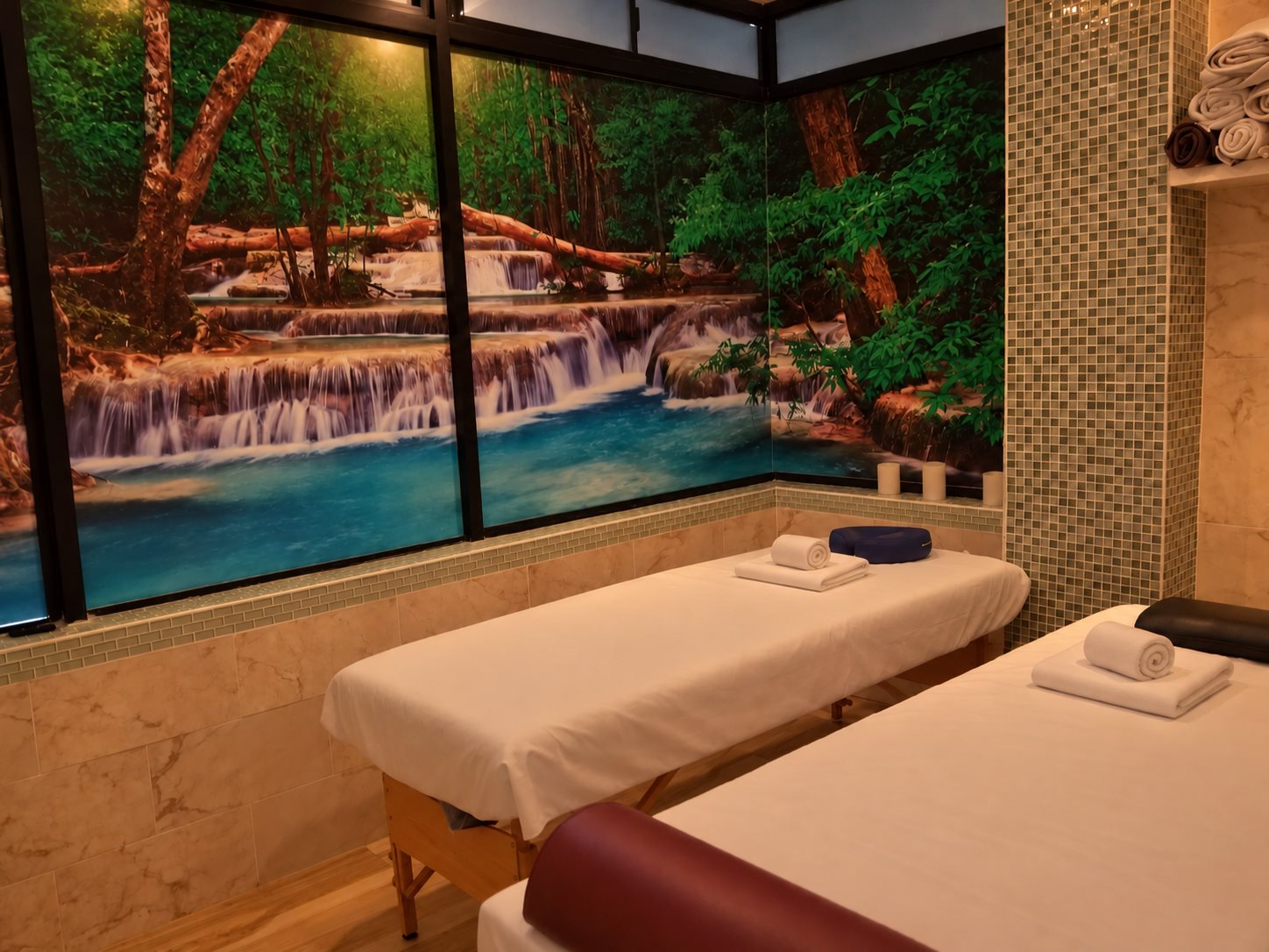 Cabina de masaje con mural de cascada, mosaicos verdes y camillas en Masaje Milagroso Spa
